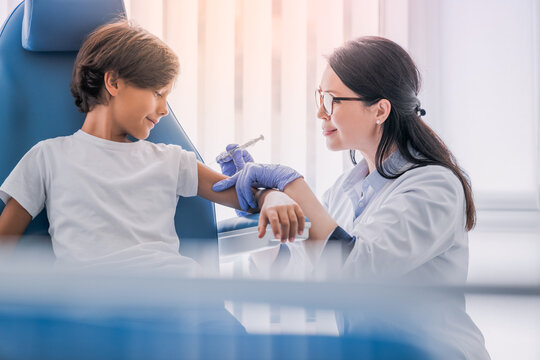 Adult doctor vaccinating patient in modern medical clinic. Small european boy kid being vaccinated against coronavirus flu influenza hepatitis tetanus in modern clinic hospital