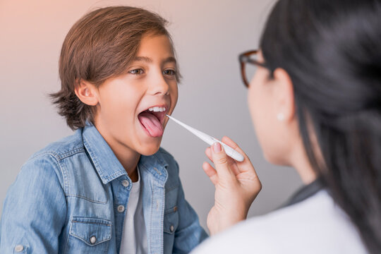 Female pediatrician using digital thermometer to check temperature of little boy. Woman doctor pediatrician measuring child fever. Cold influenza flu symptoms.