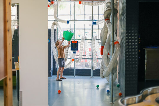 Boy holding bucket waiting for balls to eject from pipe vacuum contraption