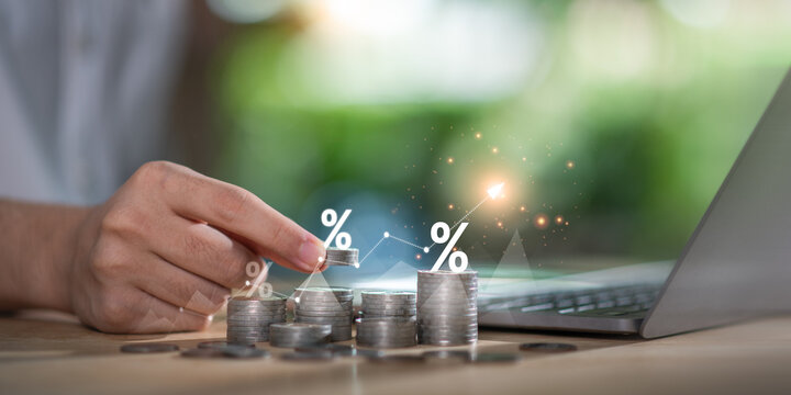 Concept of interest growth and financial investment strategy shown by a hand stacking coins with percentage icons and rising graph, interest, savings, profitability, and financial goal tracking.