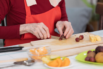 Elderly woman preparing fruit salad at home in the living room
