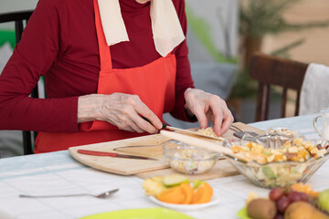 Elderly woman preparing fruit salad at home in the living room