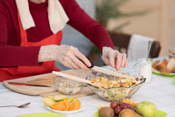 Elderly woman preparing fruit salad at home in the living room