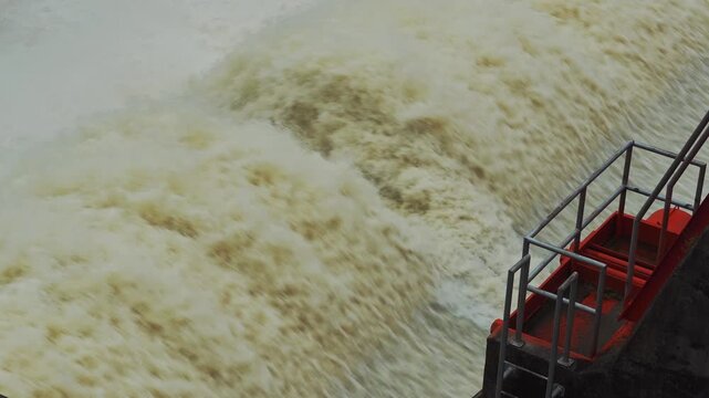 Dam floodgate with rapid water discharge, white splash and strong flow.