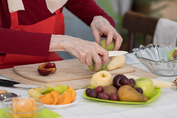 Elderly woman preparing fruit salad at home in the living room