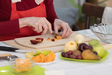 Elderly woman preparing fruit salad at home in the living room