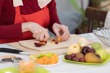 Elderly woman preparing fruit salad at home in the living room