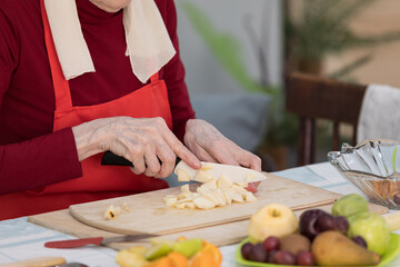 Elderly woman preparing fruit salad at home in the living room