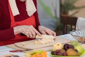 Elderly woman preparing fruit salad at home in the living room