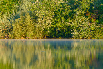 Morning landscape of a lake surrounded by trees with gentle mist rising over the water