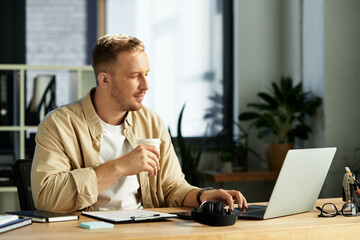 Focused young businessman works diligently in a modern office setting while enjoying a coffee