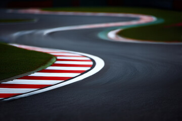 Curved racing track with red and white striped curbs on smooth asphalt and green grass beside the road under natural daylight.
