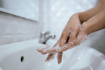 A woman washes hands with soap and water in a bathroom sink, creating bubbles and foam for hygiene, health, and cleanliness.