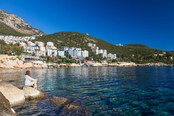 Woman looking at sea and historical town Kash placed on hills by coast of mediterranean sea in...