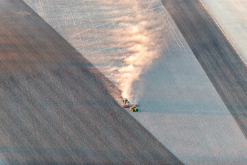 Tractor trailing dust across a dry paddock in early morning light, viewed from above