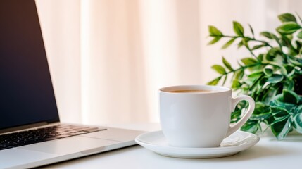 Obraz premium Cozy workspace featuring a steaming cup of tea beside a laptop with lush greenery in the background