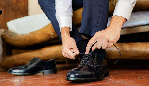 Hombre elegante ajustando los cordones de sus zapatos de vestir negros en preparación formal