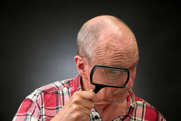 Closeup portrait of a elderly man in studio using a magnifying glass