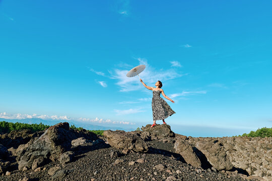 Woman in vintage dress with umbrella on volcanic rocks at Mt Etna