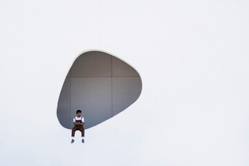 Young man sitting on wall with hole in building