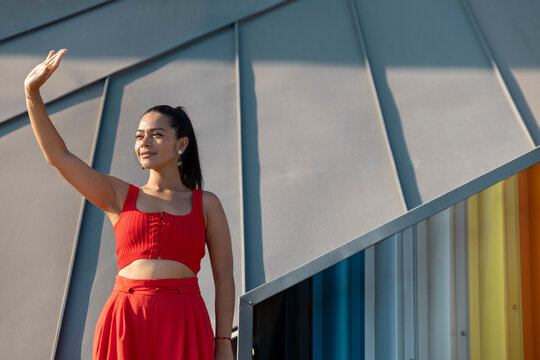 Woman in red outfit posing and waving against colorful urban background
