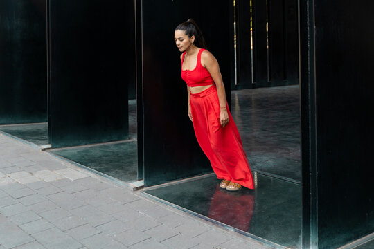 Woman in stylish red outfit posing by black modern architecture outdoors