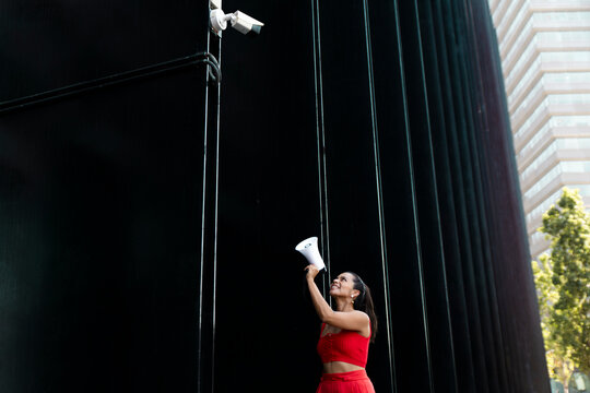 Protester shouting into megaphone at surveillance camera by black building