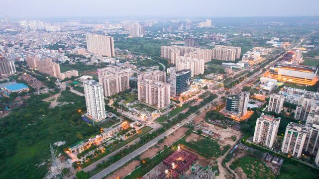 Aerial drone shot over construction site to busy street to crowded skyscraper apartment office shopping centre with small houses in between at dusk in gurgaon
