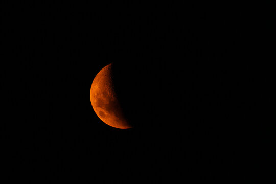 Reddish crescent moon in a dark sky