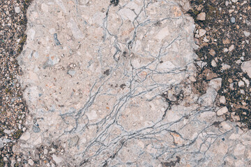 Macro photography of the texture of natural stone-cement coating with visible cracks, veins and inclusions of small stones. Light gray-beige shade, irregular structure.