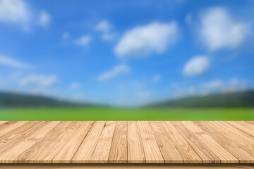 Empty perspective brown wooden board mock up display as shelf or counter bar with blurred background fresh green field and mountain range on blue sky and white clouds.