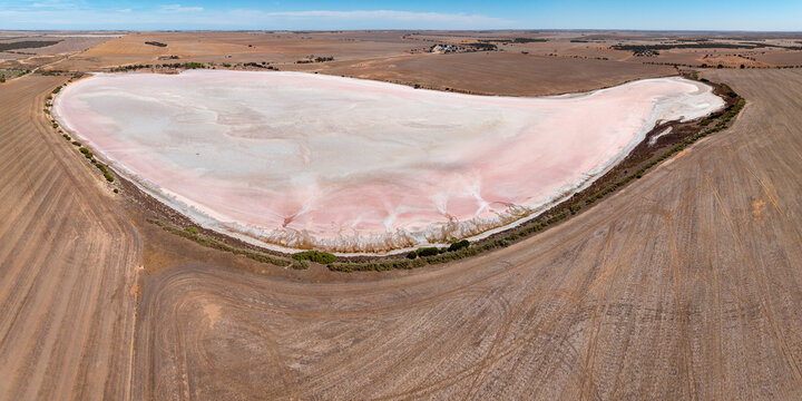 Aerial panorama of a colourful salt lake surrounded by a dry harvested field