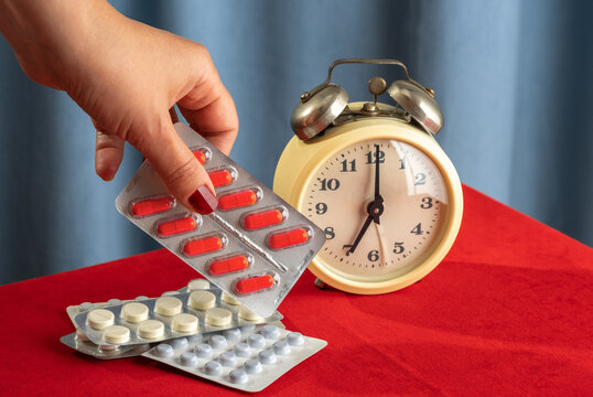 Hand holding blister pack of medication near vintage clock on red table