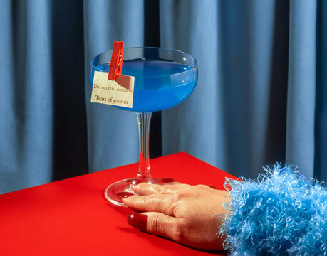 Woman with red nails and blue cocktail on red table in retro setting