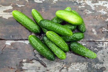 Bunch of cucumbers are sitting on a wooden table. The cucumbers are green and have a few spots on them