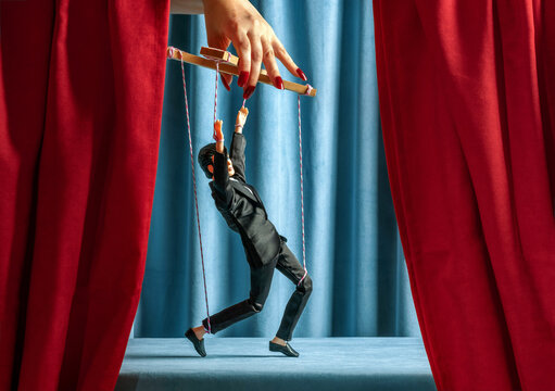 Businessman marionette controlled by a hand on theater stage