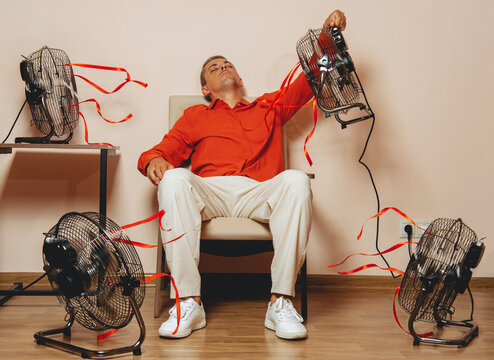 Mid adult sitting in armchair cooling down with fans during extreme heat