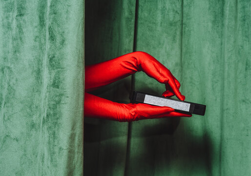 Gloved hand holding video cassette behind green curtain retro style