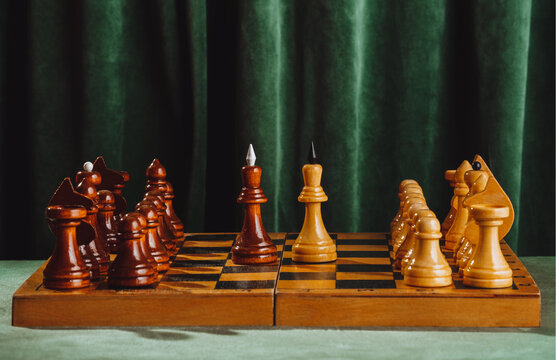 Vintage wooden chessboard with pieces against green velvet curtain