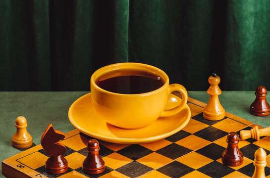 Yellow coffee cup on chessboard with vintage green velvet background