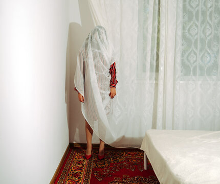 Woman behind lace curtain merging with environment in retro room