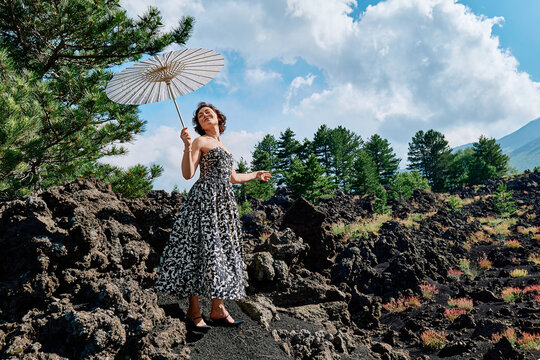 Woman in vintage dress holding umbrella on volcanic rocks of Mt Etna