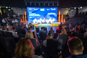Attendees at a professional conference observe a panel discussion on business topics in a modern venue.