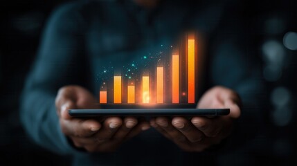 A person holds a tablet displaying a digital bar graph with glowing orange bars. The background is dark, emphasizing the graph's brightness.