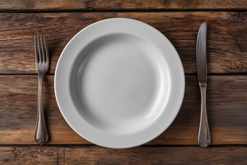 A silver fork and knife are on a wooden table with a white plate