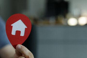 A hand holds a red location marker with a house symbol, ideal for real estate, property, and home search concepts.