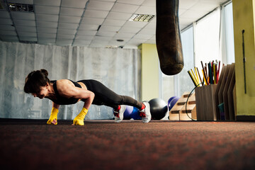 Determined female boxer doing push-ups in gym with punching bag