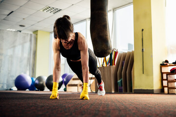 Female boxer doing push-ups in a boxing gym with yellow hand wraps