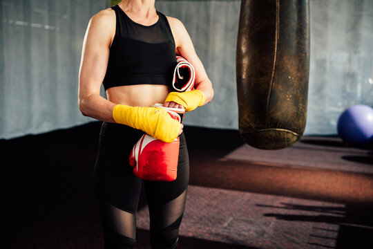 Female boxer is holding her boxing gloves and hand wraps, preparing for her intense workout session in the boxing gym, showing her dedication to the sport - Powered by Adobe