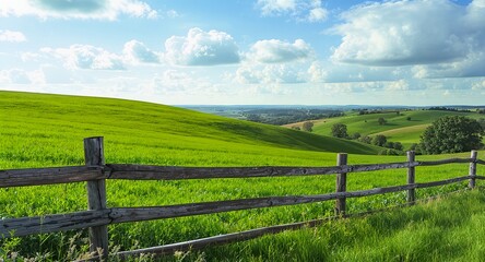 Fototapeta premium Beautiful Green Countryside Landscape with Rolling Hills and Wooden Fence under Blue Sky